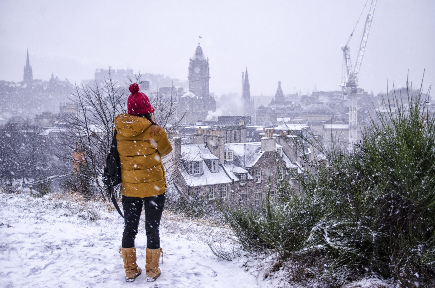 An Edinburgh tourist overlooking Edinburgh's skyline at Christmas in the snow